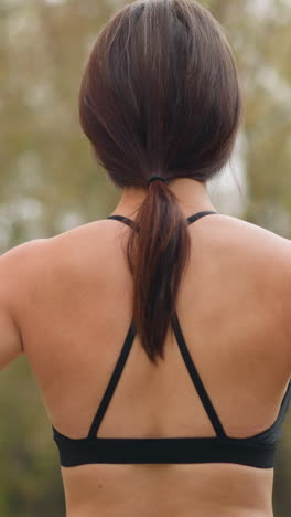 back view of a lady wearing black singlet and leggings, standing outdoors with hands placed on her waist, showcasing a confident posture, athletic physique, and relaxed demeanor in a natural setting