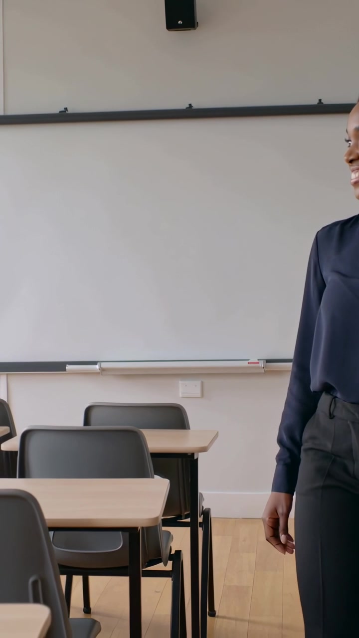 Video verticale: Insegnante sorridente con maglia blu navy che fa un passo a sinistra dopo una panoramica della telecamera in classe, spazio per il testo