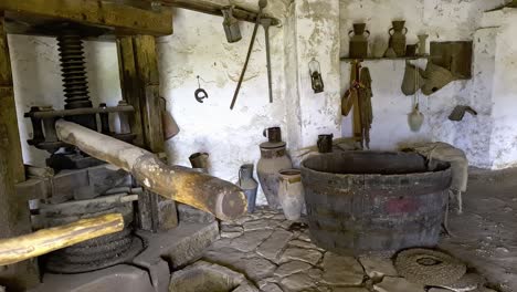 Tilt-up-of-old-olive-oil-press-and-tub-with-rusty-utensil-hanged-on-wall-at-Mangiapane-village-in-Sicily,-Italy