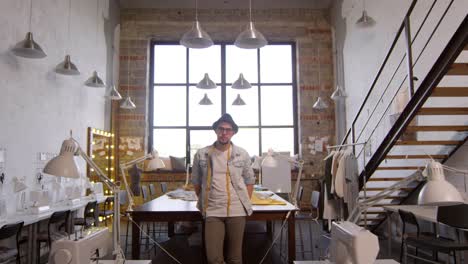 zoom in of male fashion designer posing for camera in sewing workshop