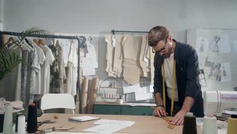 young male designer in eyeglasses in the workshop measure pieces of clothes in studio