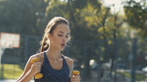 Chica-Deportiva-Haciendo-Ejercicio-De-Golpes-Con-Mancuernas-En-La-Cancha-De-Baloncesto-Al-Aire-Libre-En-La-Mañana-De-Verano