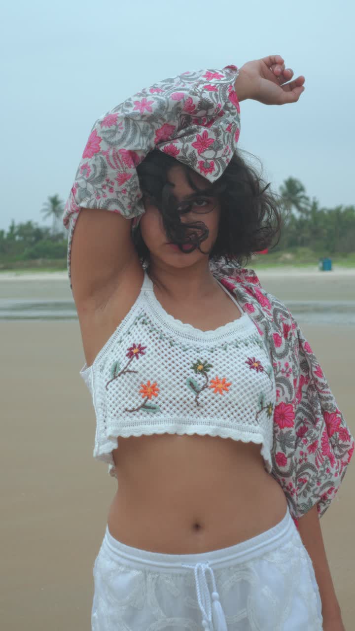 Young woman posing confidently on a sandy beach, wearing casual summer clothing, with wind-blown hair and a relaxed yet expressive mood, captured in soft natural light
