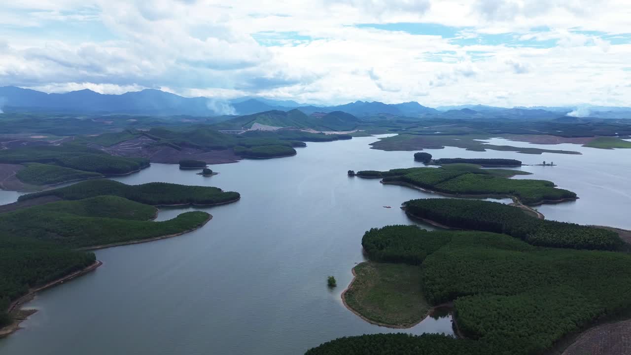 Drone zooms out showing large Vietnamese lake with surrounding vegetation, scattered clouds and hills