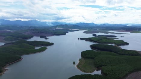 drone zooms out showing large vietnamese lake with surrounding vegetation, scattered clouds and hills