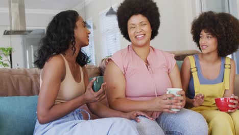 happy diverse female friends sitting on sofa in living room, talking and smiling