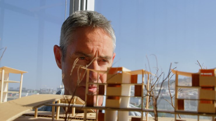 Vorderansicht männlicher Architekten, die ein Gebäudemodell im Büro betrachten 4K