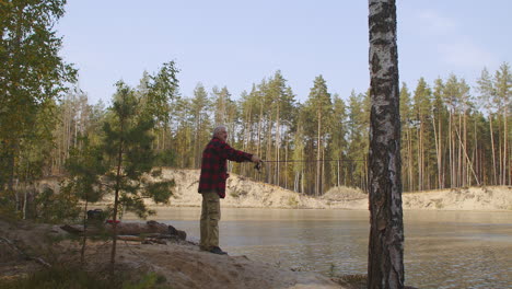 Ein-Entspannter-Mann-Genießt-Das-Angeln-An-Einem-ökologischen-Ort-Und-Wirft-Die-Rute-Im-Wasser-Eines-Sauberen-Sees,-Ruht-Sich-Allein-Im-Wald-Aus-Und-Erholt-Sich