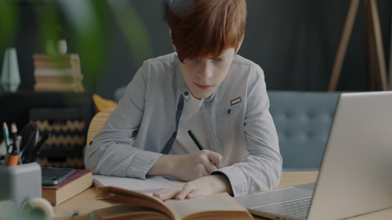 Teenage boy studying at home with laptop and notebook