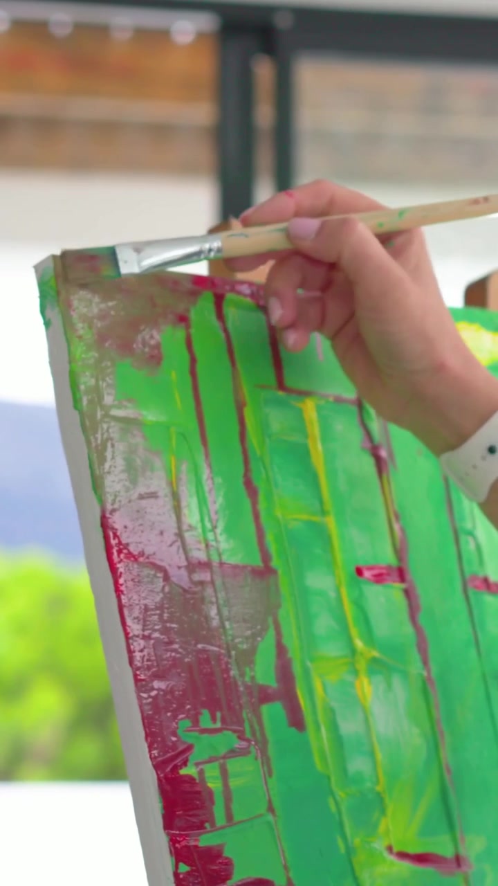 Video verticale: Artista in denim che si allunga creando una griglia magenta su tela verde in studio, con spazio per il testo.