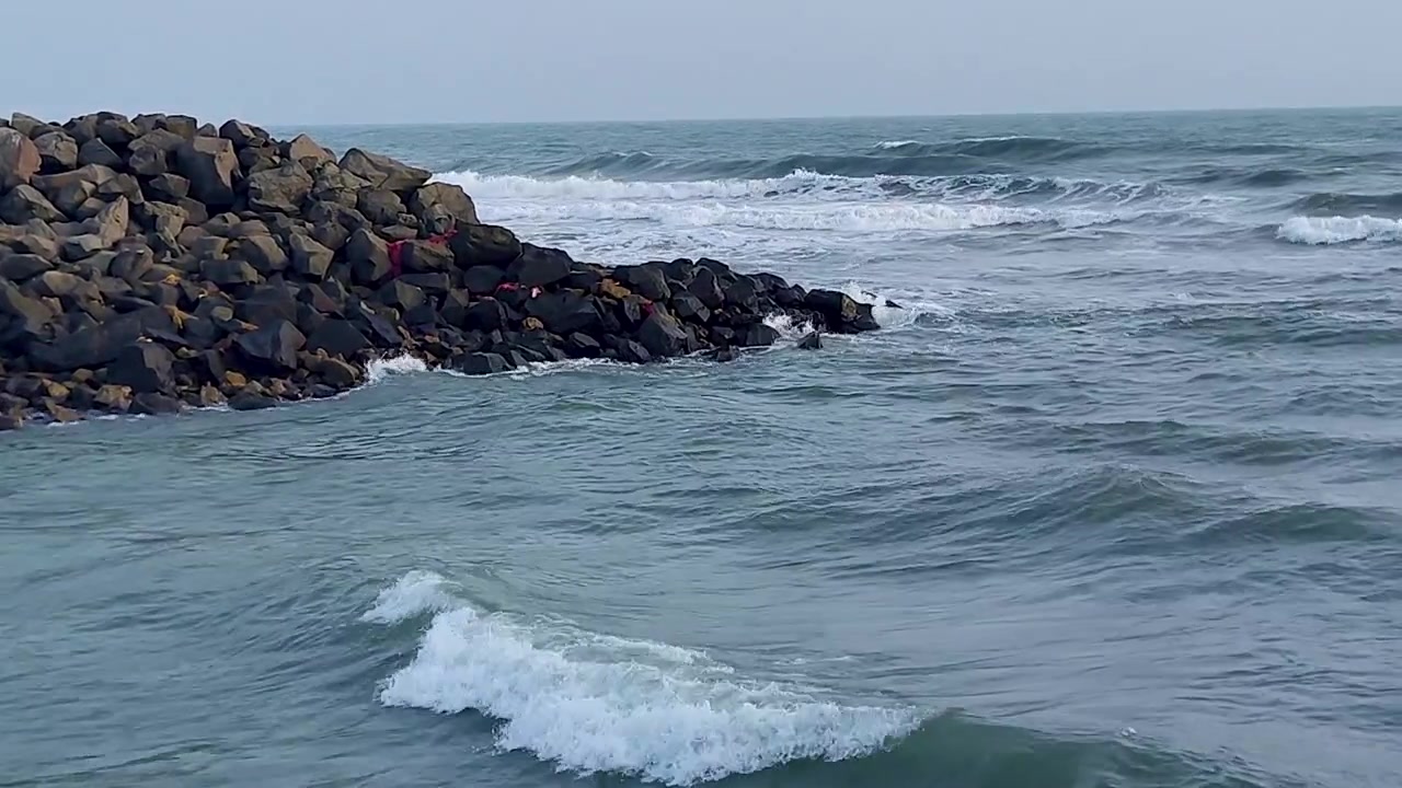 Onde oceaniche che si infrangono su un frangiflutti roccioso a Gomti Ghat, Dwarka. Perfetto per documentari sui pellegrinaggi indù, fiume sacro che incontra il mare, turismo costiero del Gujarat e contenuti sul viaggio spirituale