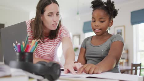 une femme blanche heureuse et sa fille afro-américaine font leurs devoirs ensemble.