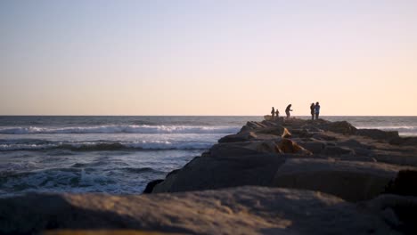 Beautiful,-calm-and-peaceful-sunset-in-San-Diego,-shooting-down-a-jetty-with-people-and-waves-crashing-alongside-it