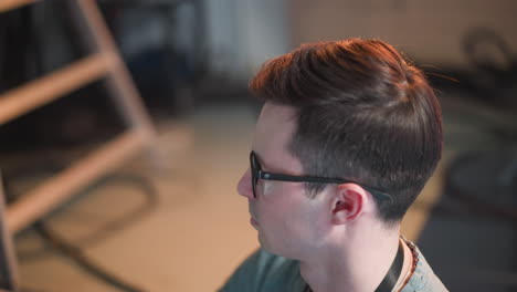 person working in tv studio, focused on monitor and video equipment. wearing glasses, seated while adjusting broadcast settings, with studio lights and cables in background