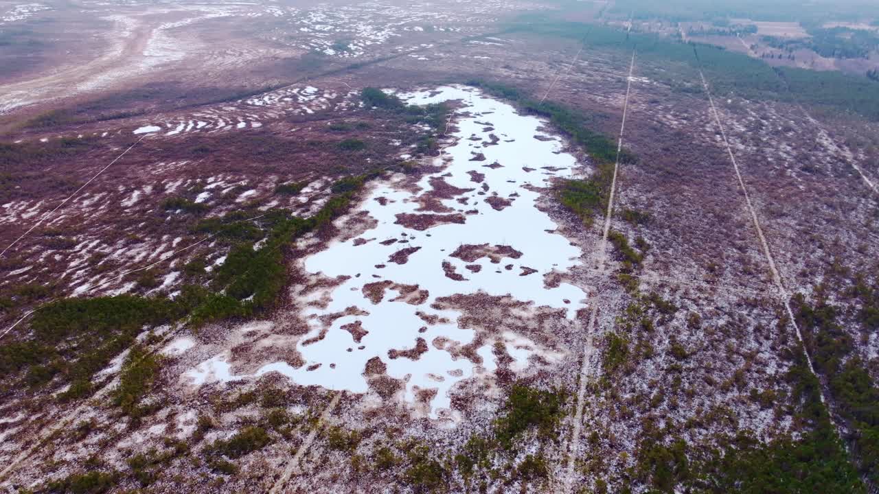High altitude aerial view of frozen bog lake and snowy peatlands, Cenas Tīrelis