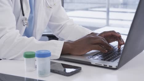 hands of african american male doctor using laptop in hospital office, slow motion