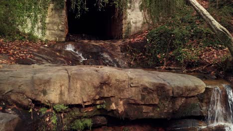 Rocky-creek-falls-leading-to-dark,-overgrown-tunnel