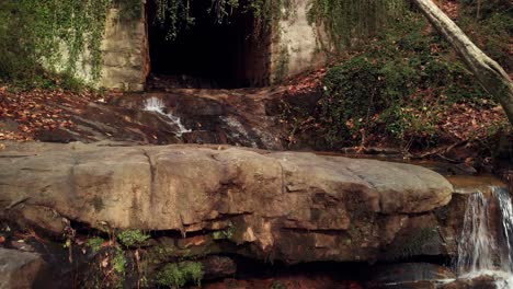 Felsige-Bachfälle,-Die-Zu-Einem-Dunklen,-überwucherten-Tunnel-Führen