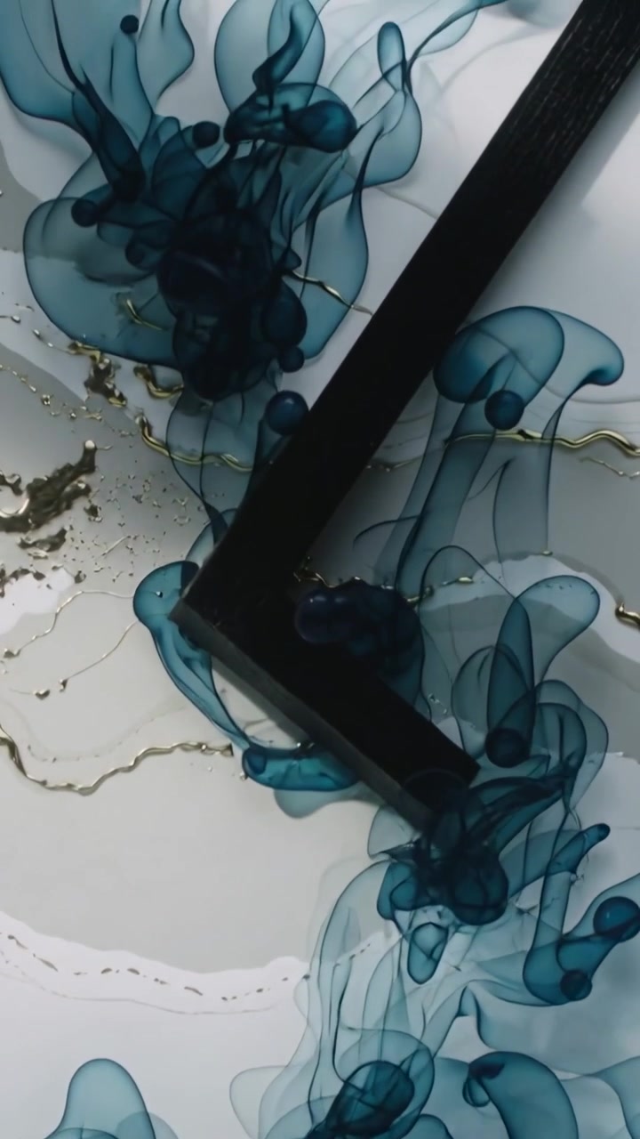 Video verticale: Pennacchi di colorante verde acqua che si formano su un tavolo con striature dorate mentre uno strumento nero a forma di L viene inserito