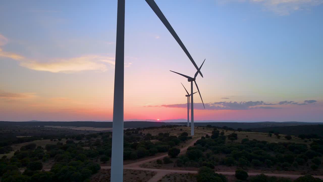 카메라는 낮은 태양을 배경으로 숲에서 풍력 터빈 농장 실루엣을 보여주기 위해 뒤로 물러납니다.