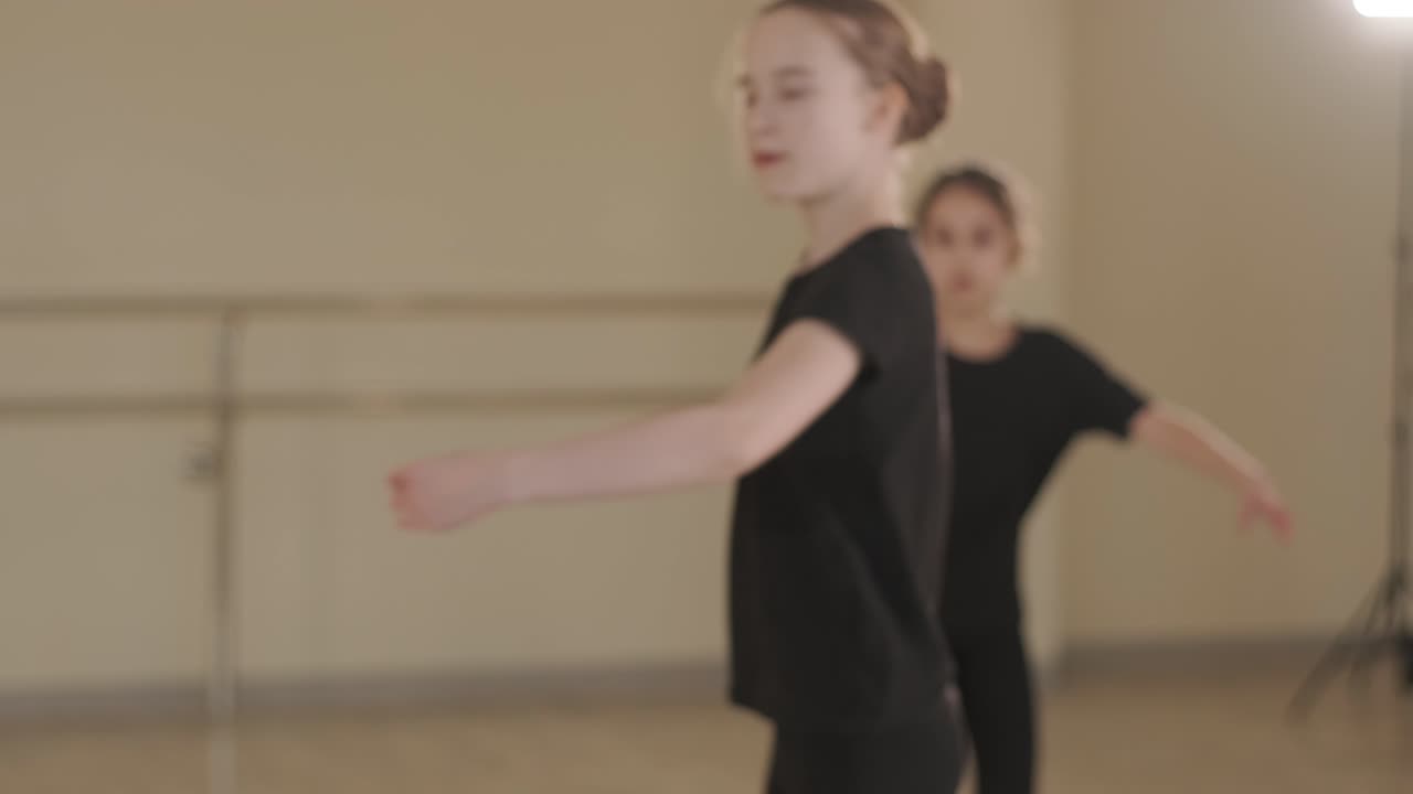 Un gruppo di giovani allievi di danza classica in abbigliamento da ballo nero che eseguono esercizi in un ampio studio di danza con pavimenti in legno e barre a muro. Espressioni concentrate e movimenti sincronizzati