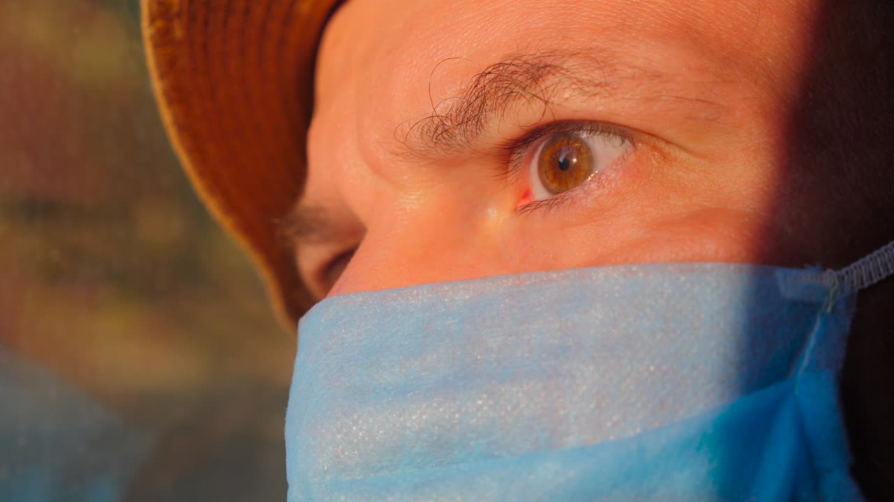 giovane con una maschera protettiva mentre viaggia in treno, autobus, auto. luce solare sul viso del passeggero. emozioni facciali dell'uomo viaggiatore. concetto di vacanza durante la pandemia di coronavirus covid-19