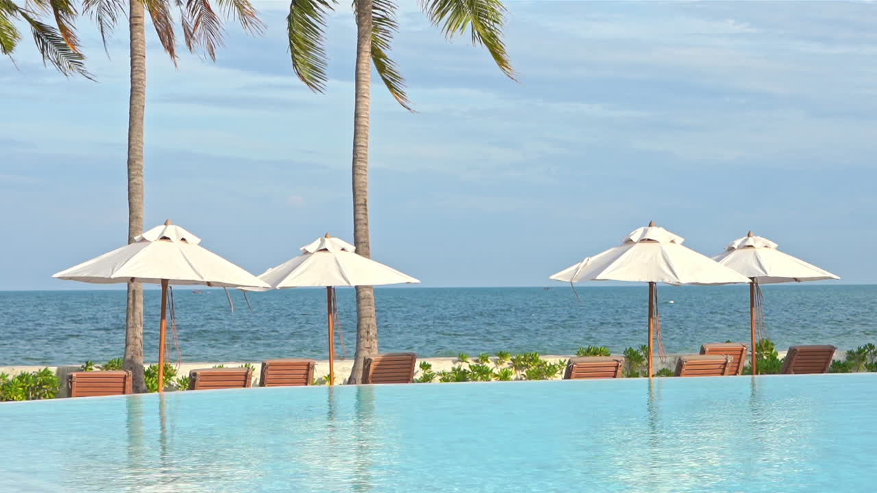 vistas al mar con sombrillas blancas y salones de madera vacíos cerca de la piscina en la playa sin gente en el marco