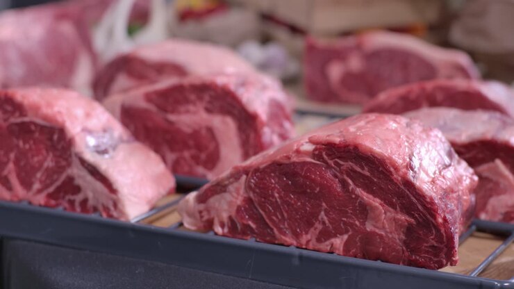 Close up of several thick-cut raw marbled ribeye beef steaks resting on a metal rack in a professional kitchen or butcher shop