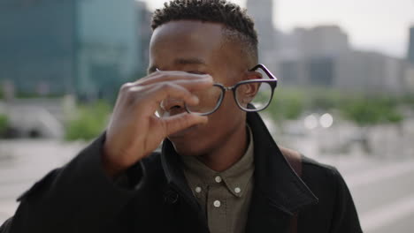 close up portrait of young trendy african american man student looking serious at camera confident removes glasses in city background