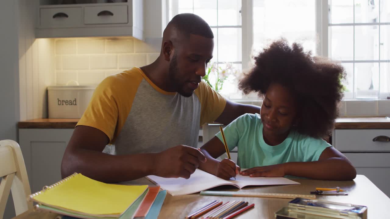 Figlia afroamericana e suo padre che fanno insieme i compiti al tavolo della cucina.
