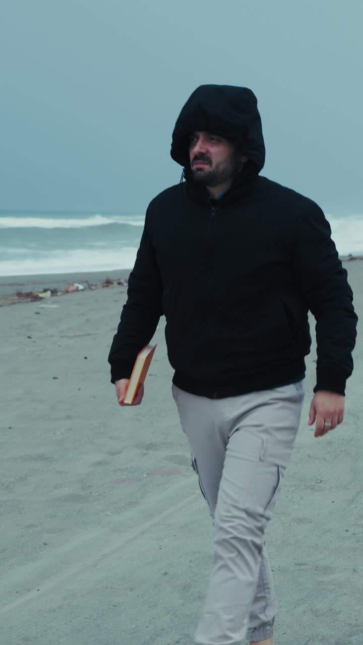 Man At The Sea In Winter Puts On His Hood To Protect From The Wind