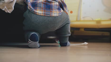 funny kid plays on knees at bed on wooden floor backside