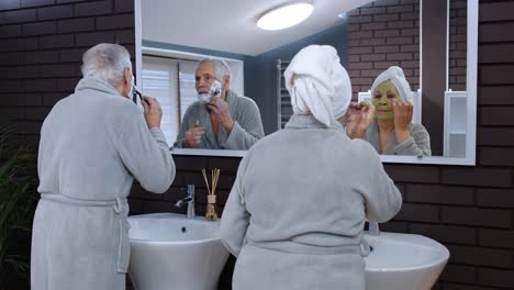 senior grandmother applying facial mask and grandfather shaving with manual razor blade at bathroom