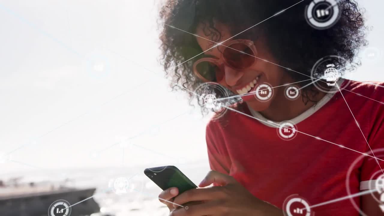 Network of digital icons against african american woman using smartphone at the beach