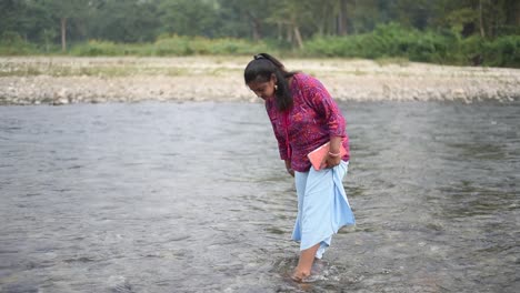 Una-Joven-India-Gordita-Y-Saludable-Está-Parada-En-La-Orilla-Del-Río-Y-Jugando-Con-Agua,-A-Cámara-Lenta