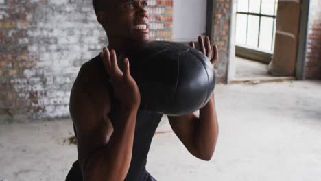 shirtless african american man exercising with medicine ball in an empty urban building