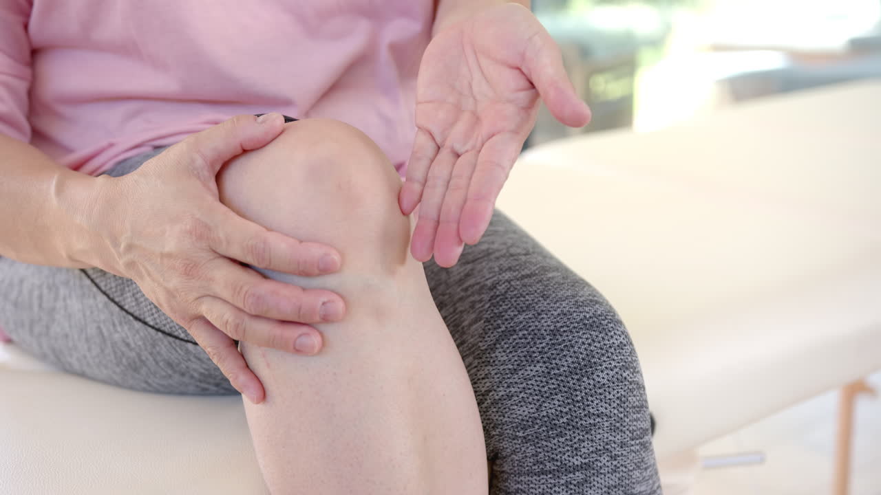 Senior asian woman holding knee, explaining pain during physiotherapy session at home