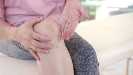 senior asian woman holding knee, explaining pain during physiotherapy session at home