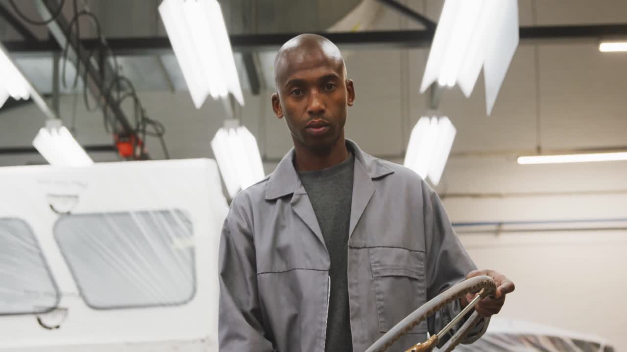 African American male car mechanic holding a steering wheel and looking at the camera