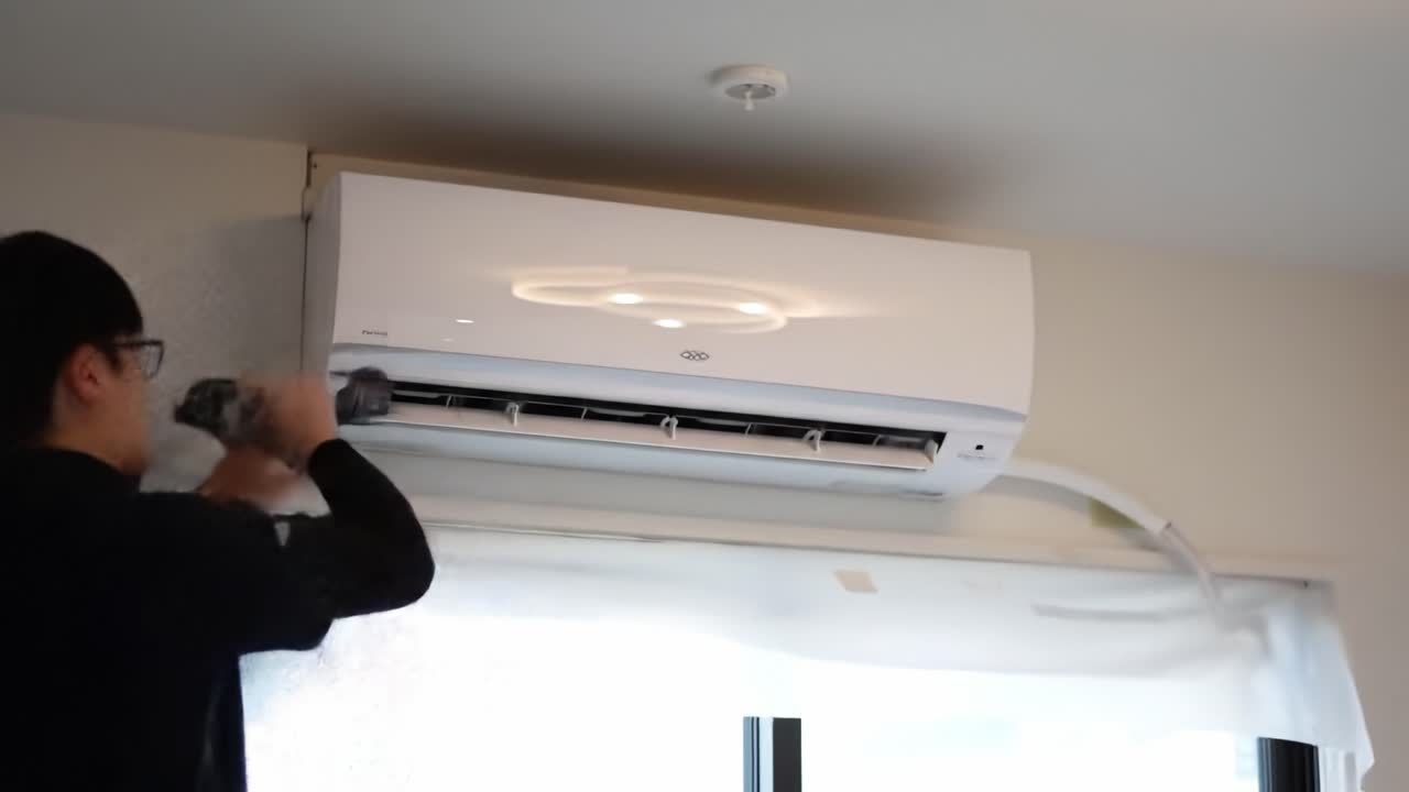 A technician carefully installs a new air conditioning unit in a stylish apartment. Tools are gathered nearby, and natural light fills the room, enhancing the modern decor.