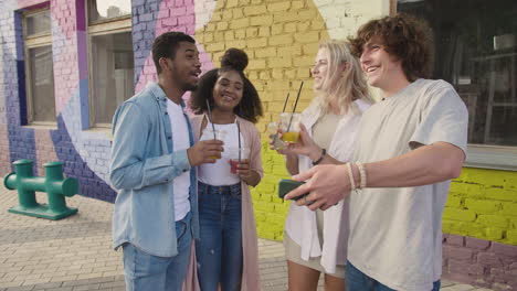 grupo de jóvenes amigos tomando selfies juntos y divirtiéndose al aire libre, mientras sostienen sus bebidas frescas en vasos de plástico 1