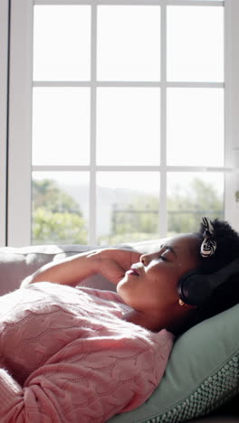 vertical video of happy african american woman singing and listening music on headphones at home