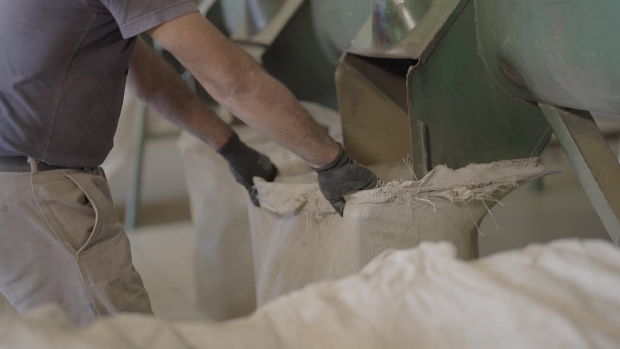 Close-up of a worker lifting a white bag to position it for machine filling at a yerba mate factory.