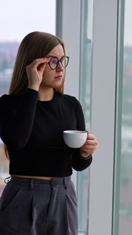 Beautiful female with cup of coffee standing by the window Vertical video
