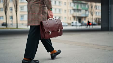 midsection businessman going to work by walk he has a leather briefcase in his hand. commuting to the office. public transport