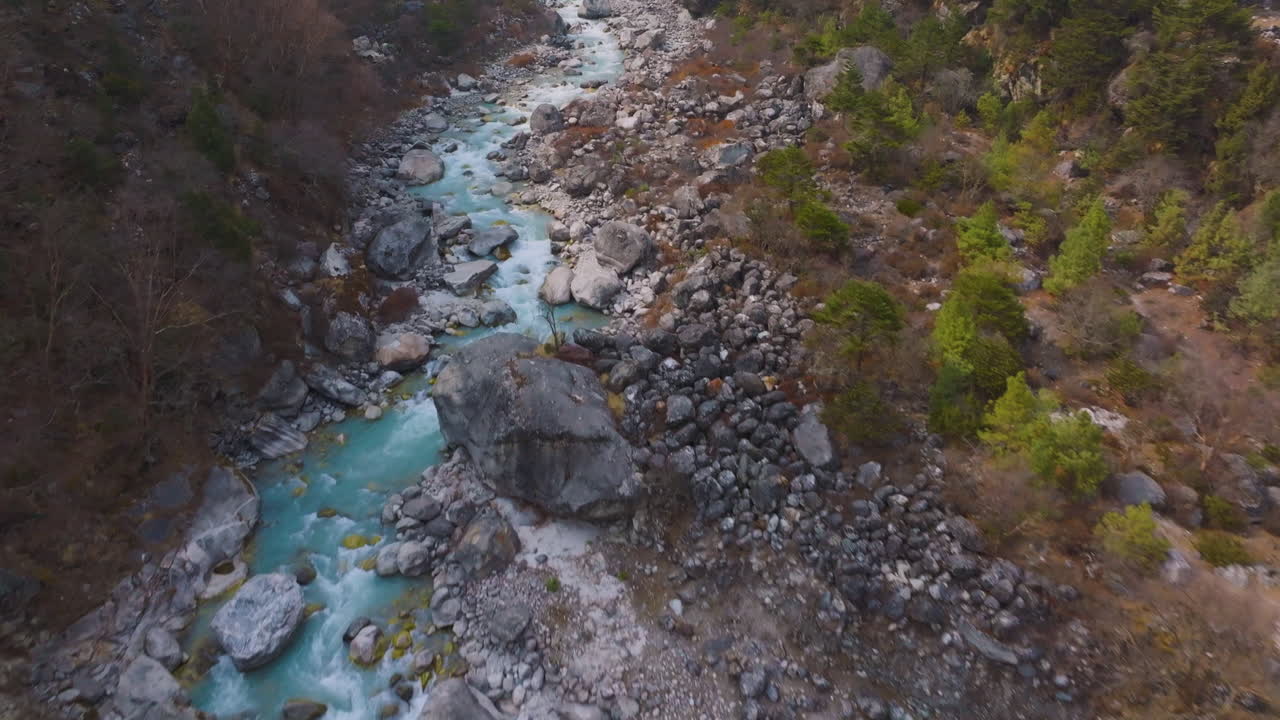 Drone shot of snow-melt river at Everest region, Trekking trails with bridge, greenery on banks and scenic hilly landscape