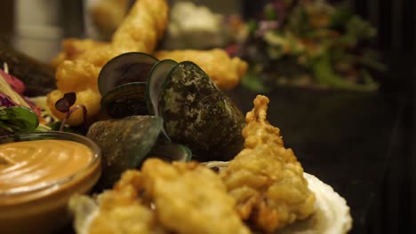 Chef-finishing-dish-New-Zealand-Greenshell-mussells-on-plate-with-green-salad,-oysters-and-gravy---CLOSE-UP