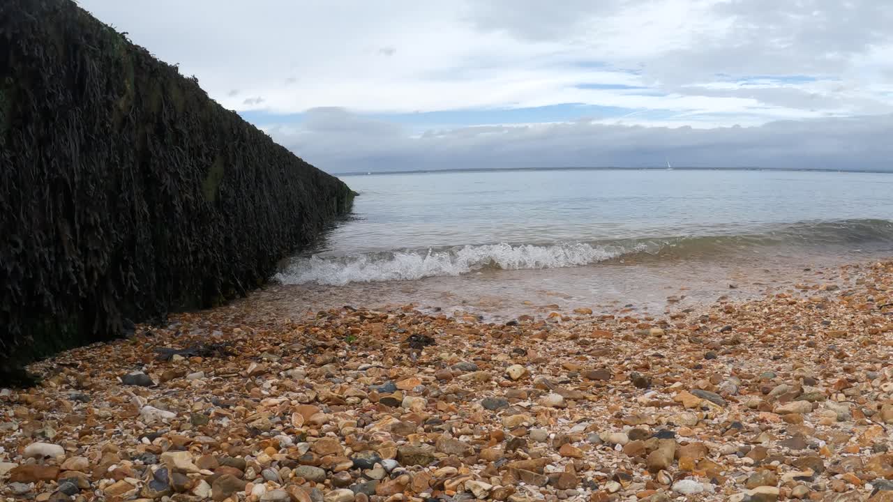 las olas de agua cristalina besan suavemente la playa de guijarros naranja en la isla de wight.