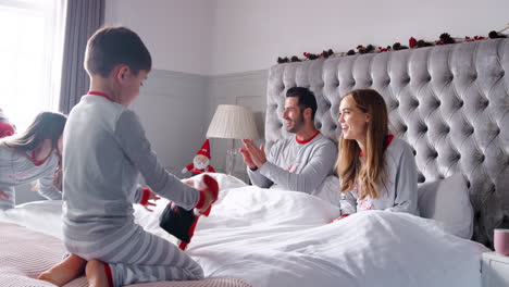 excited children running into parents bedroom at home with stockings as family open gifts on christmas day