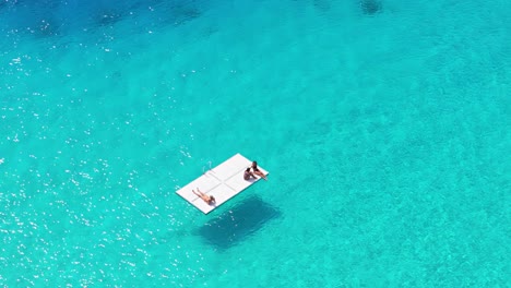 couple and friends relax on floating pad in middle of serene crystal clear blue caribbean waters